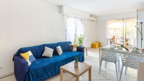 A modern living room with a blue sofa, a small table, and a dining area with a glass table and chairs.