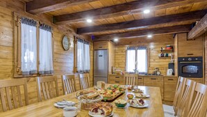 L’intérieur d’un chalet en bois présente une table à manger dressée pour un repas, des chaises en bois, un coin cuisine équipé d’appareils électroménagers et une décoration rustique.