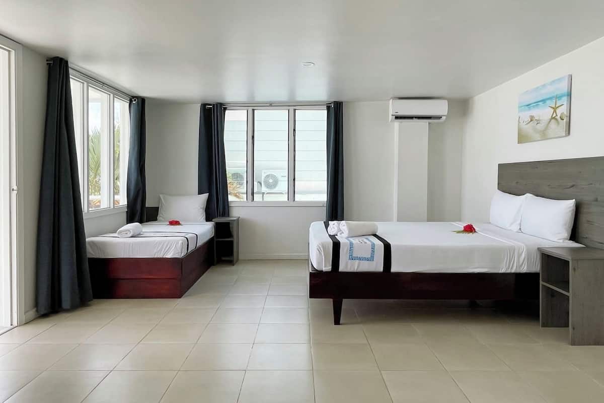 A hotel room with two beds, a large window, an air conditioning unit, and a painting on the wall.