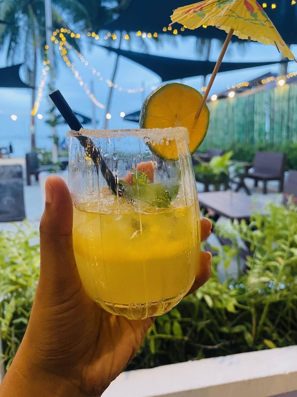 Eine Hand hält ein Cocktailglas mit einer Limettenscheibe und einem Strohhalm.
