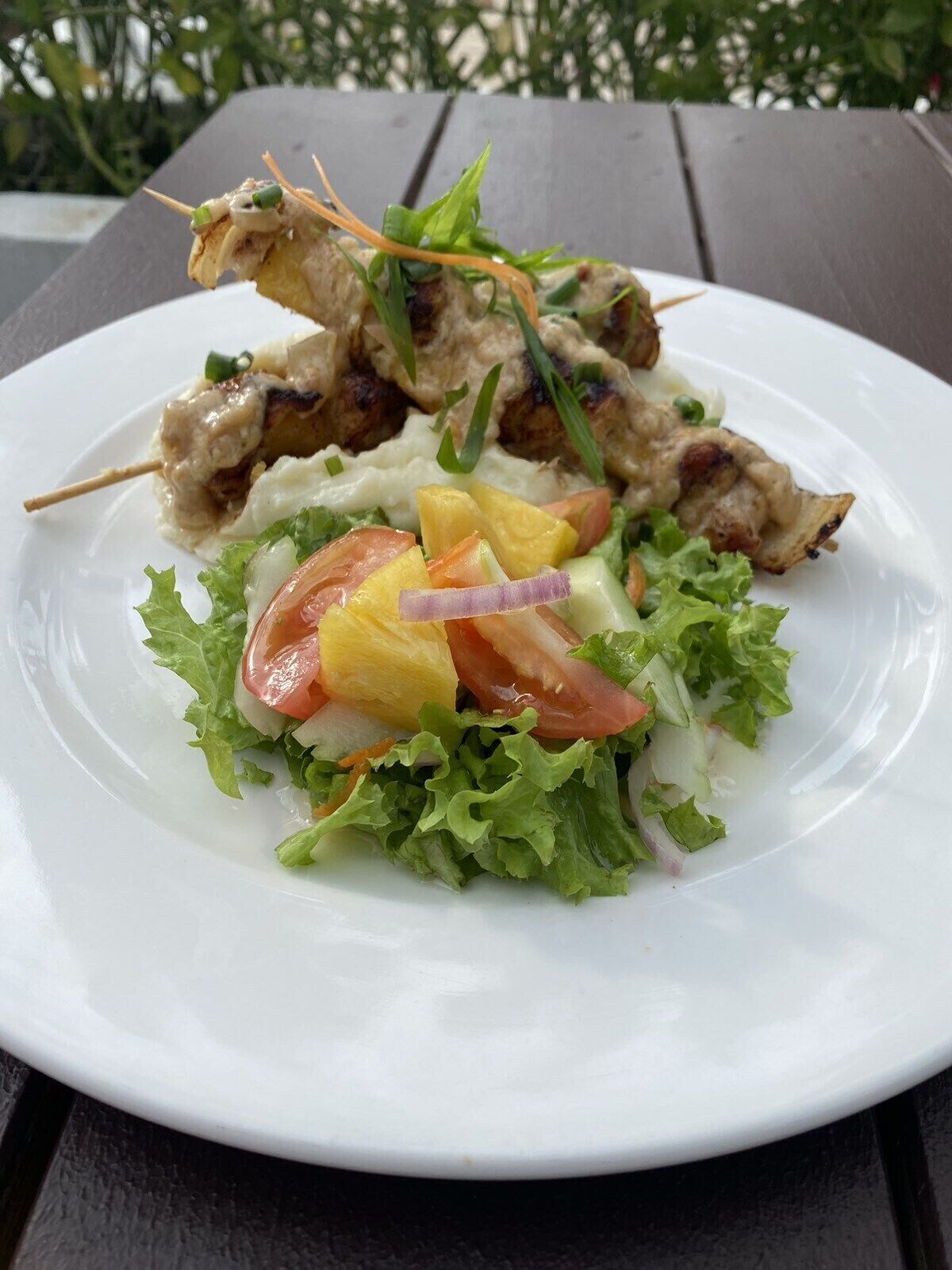 A plate of grilled chicken skewers with a side salad of lettuce, tomatoes, and pineapple.