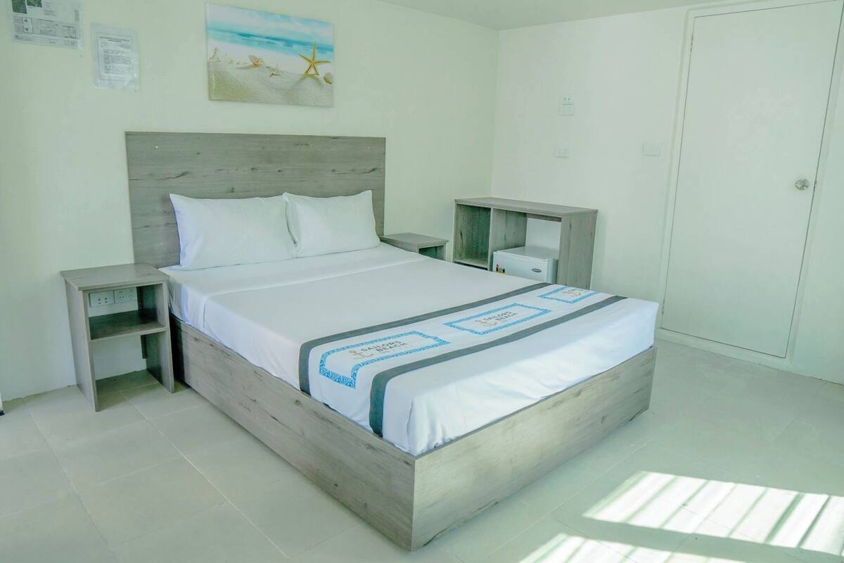 A neatly arranged bedroom with a wooden bed, white bedding, and a small bedside table with a lamp.