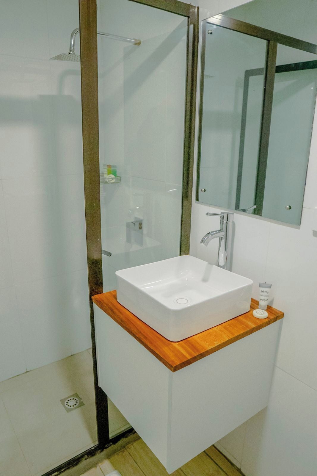A bathroom with a glass-enclosed shower, a white sink with a wooden countertop, and a mirror above the sink.