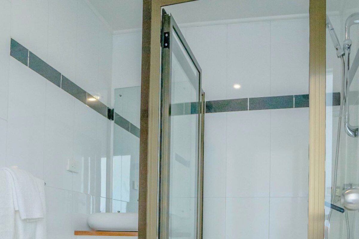 A modern bathroom with a glass-enclosed shower, white tiles, and a wooden vanity.