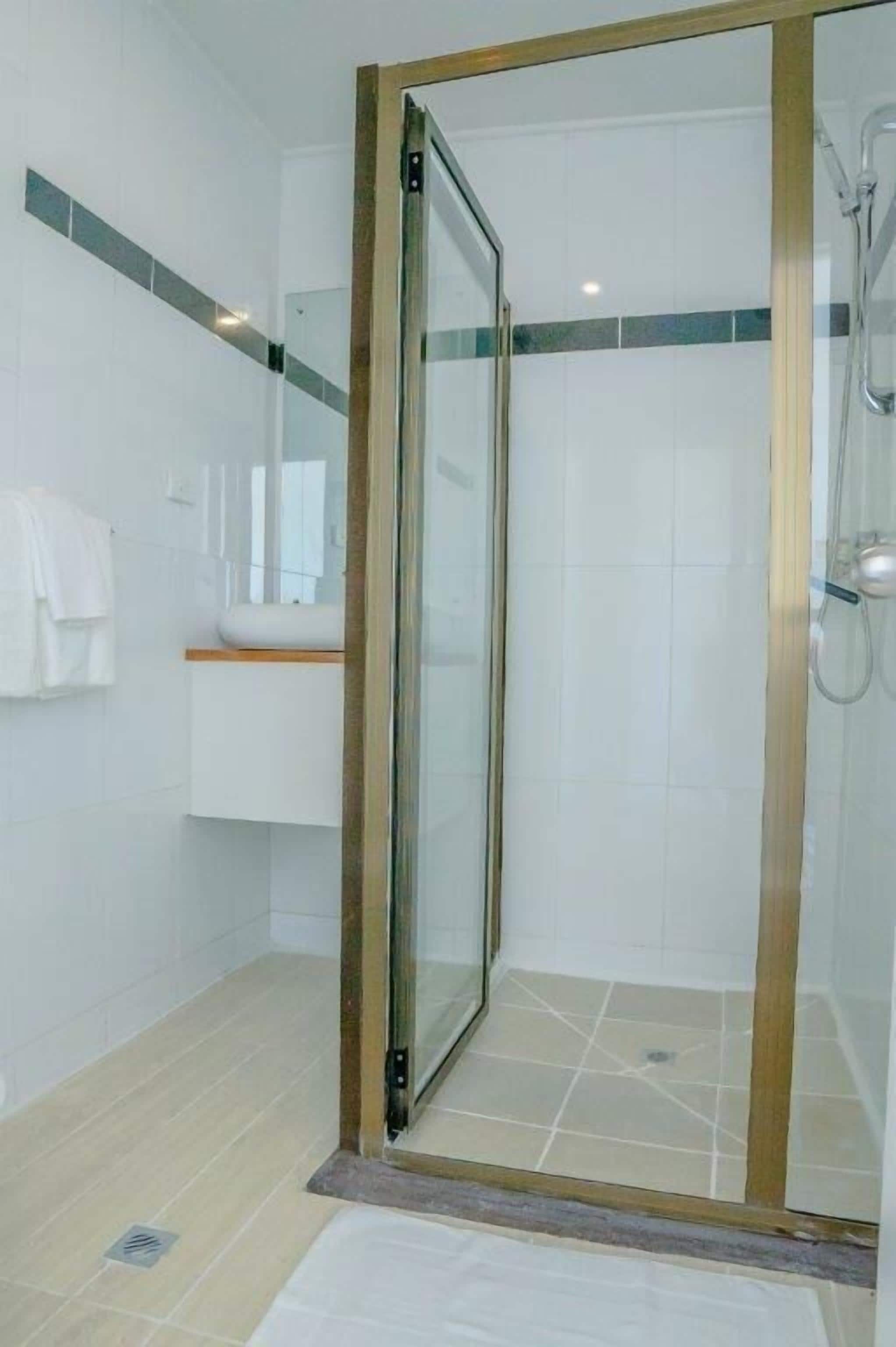 A modern bathroom with a glass-enclosed shower, white tiles, and a wooden vanity.