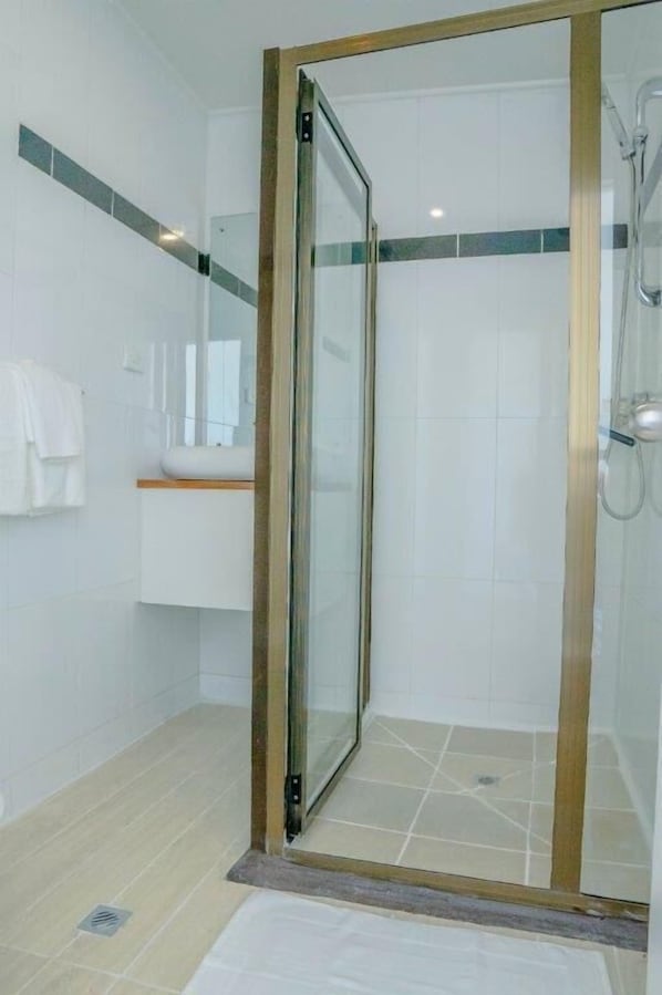 Un baño moderno con ducha de mampara de vidrio, azulejos blancos y tocador de madera.