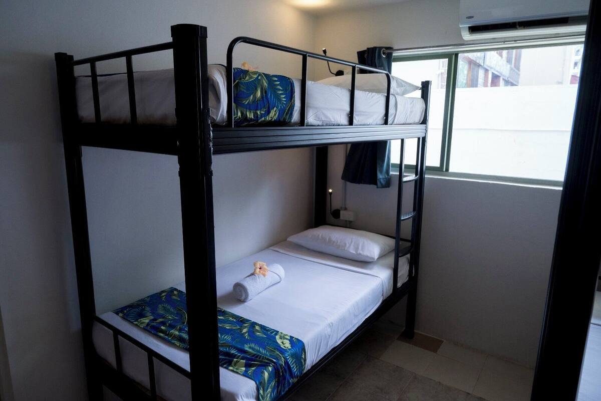 A bunk bed room with a window, a small table, and a wall-mounted air conditioner.