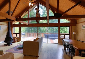 A spacious living area with a high ceiling, large windows, a fireplace, and a dining table.