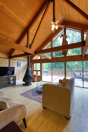 A spacious living room with a fireplace, wooden beams, large windows, and a television.