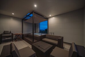 A modern, well-lit outdoor living area with a built-in hot tub, seating arrangements, and a view of the sky.