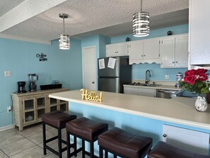 A kitchen with a bar area, a refrigerator, a coffee maker, and a 'Hello!' sign.