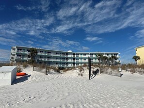 A beachfront hotel with multiple balconies, a sandy beach in front, and a clear sky.