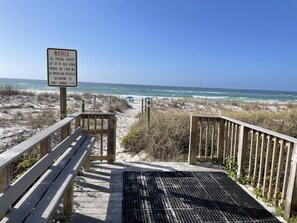 A wooden boardwalk leading to a beach with a notice sign.