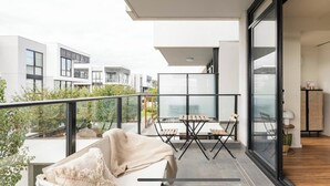 Ein Balkon mit Tisch und Stühlen, Blick auf benachbarte Gebäude und eine Glastür zu einem Innenraum mit einer Küche.