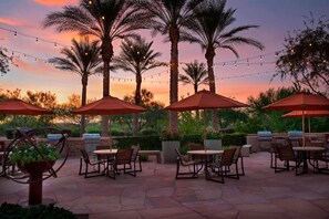 Un patio al aire libre con mesas y sillas, luces colgantes y sombrillas.