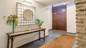 A reception area with a wooden console table, two potted plants, a wall-mounted decorative piece, and a wooden door labeled "SALIDA".