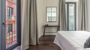 Ein Schlafzimmer mit Bett, einem kleinen Tisch, einem Spiegel und Blick auf einen Balkon.