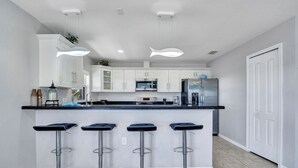 A modern kitchen with white cabinets, a black countertop, and three bar stools. - Dock, Pool, FREE RAMP, Kayaks, Jacuzzi, Amazing Ocean Views Pets are Welcomed! (Marathon)