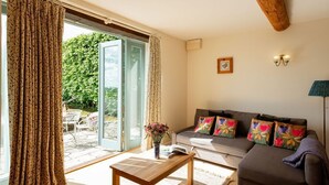 A living room with a sofa, a coffee table, and a large window with curtains. - Two Bedroom Family Friendly Holiday Cottage in the Cotswolds - Will's Cottage (Stroud)