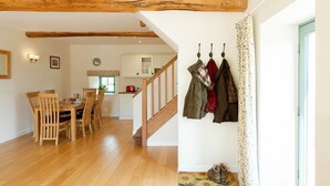 A dining area with wooden chairs and a table, a staircase leading to an upper level, and a coat rack with hanging items. - Two Bedroom Family Friendly Holiday Cottage in the Cotswolds - Will's Cottage (Stroud)