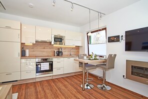 Une cuisine moderne avec des meubles blancs, des appareils en acier inoxydable, un plan de travail en bois et un coin bar avec des tabourets.