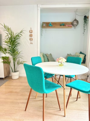 Un coin repas avec une table ronde, des chaises de couleur turquoise et une plante en pot.
