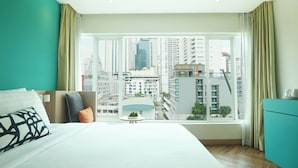 A modern hotel room with a large bed, a small table with a plant, and a view of the cityscape through large windows. - SQ Boutique Hotel (Bangkok)