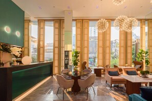 A modern hotel lobby with a reception desk, seating area, and large windows offering city views. - SQ (Bangkok)