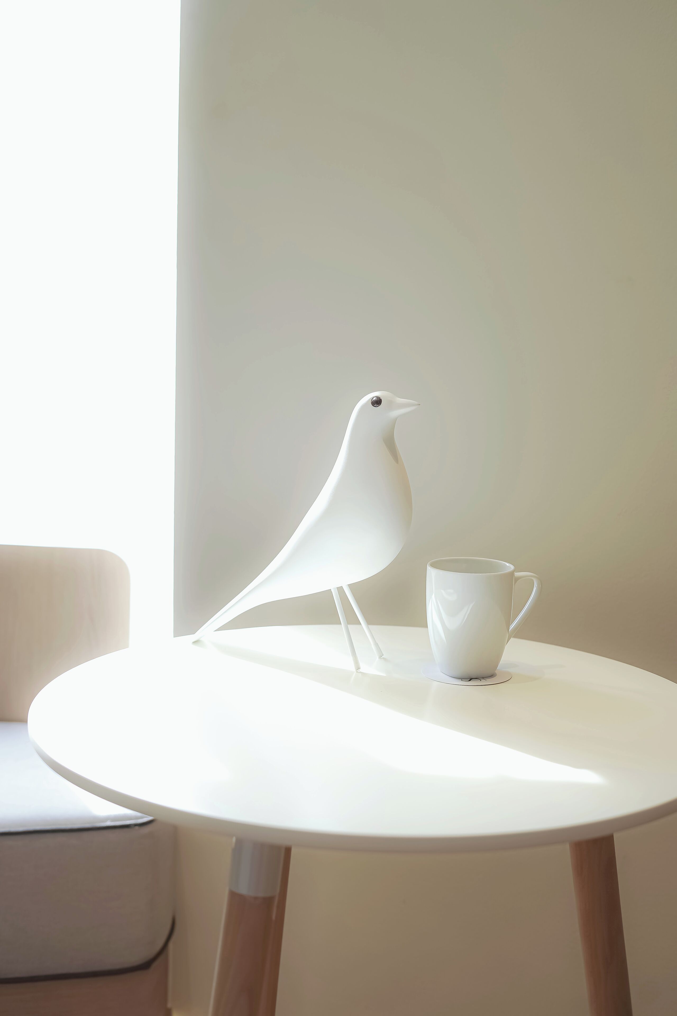 A white bird figurine and a white mug on a round table.