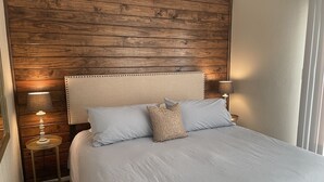 A bedroom with a wooden headboard, a bed with light blue bedding, two bedside lamps, and a small table with a lamp. - Waterfront Terramar Getaway, Amazing Sunsets, Outdoor Bar, Kayak, Beach, Fishing (Galveston)