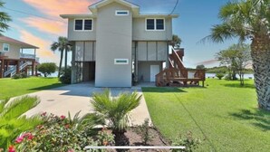 A two-story house with a front porch, a staircase leading to the upper level, and a well-maintained lawn. - Waterfront Terramar Getaway, Amazing Sunsets, Outdoor Bar, Kayak, Beach, Fishing (Galveston)