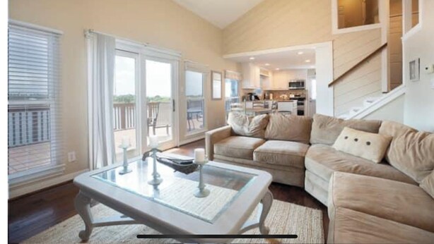 A spacious living room with a glass coffee table, beige sofas, and a view of the outdoor balcony. - Waterfront Terramar Getaway, Amazing Sunsets, Outdoor Bar, Kayak, Beach, Fishing (Galveston)