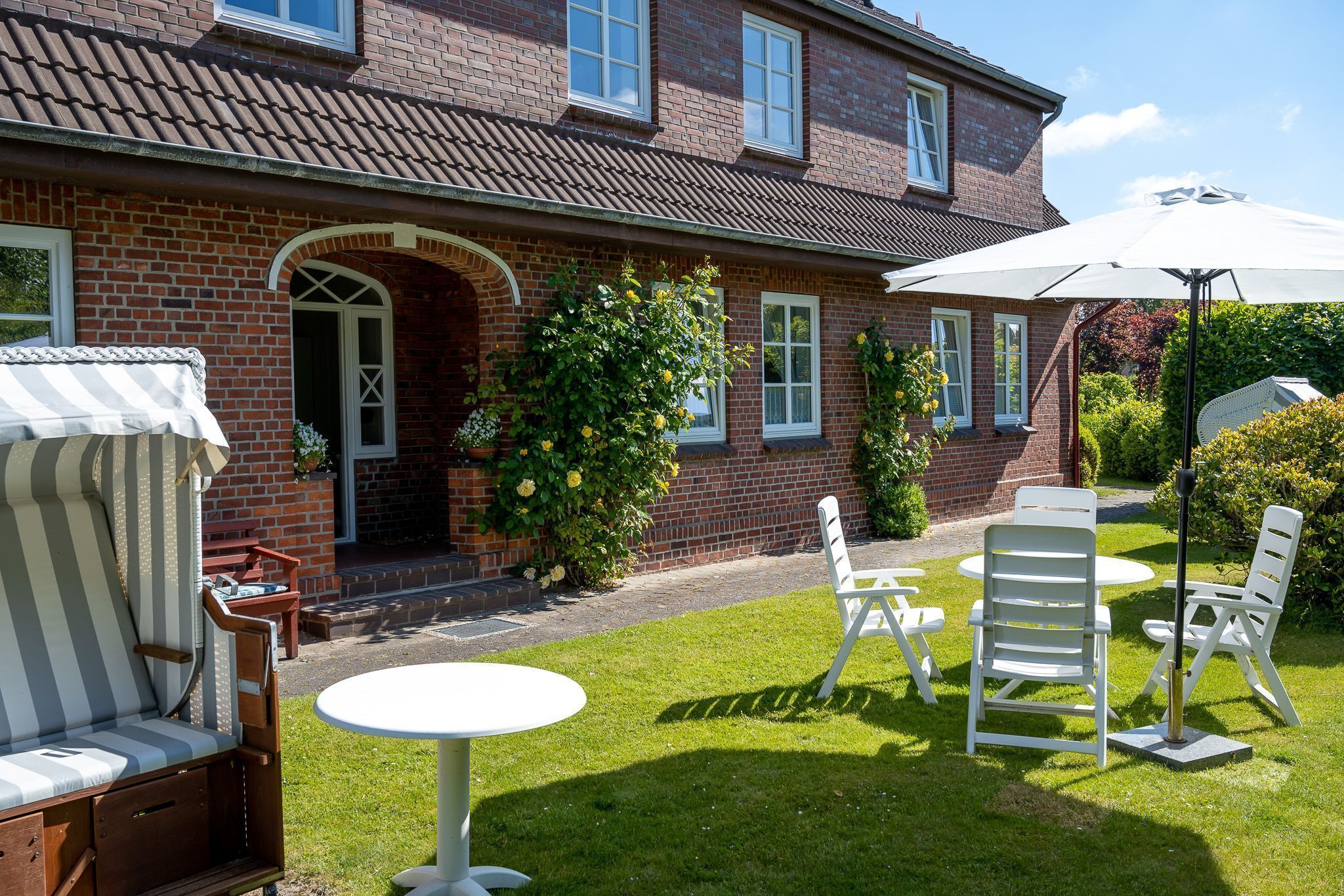 Une maison en briques avec un patio aménagé dans le jardin, comprenant des meubles d’extérieur et une table.
