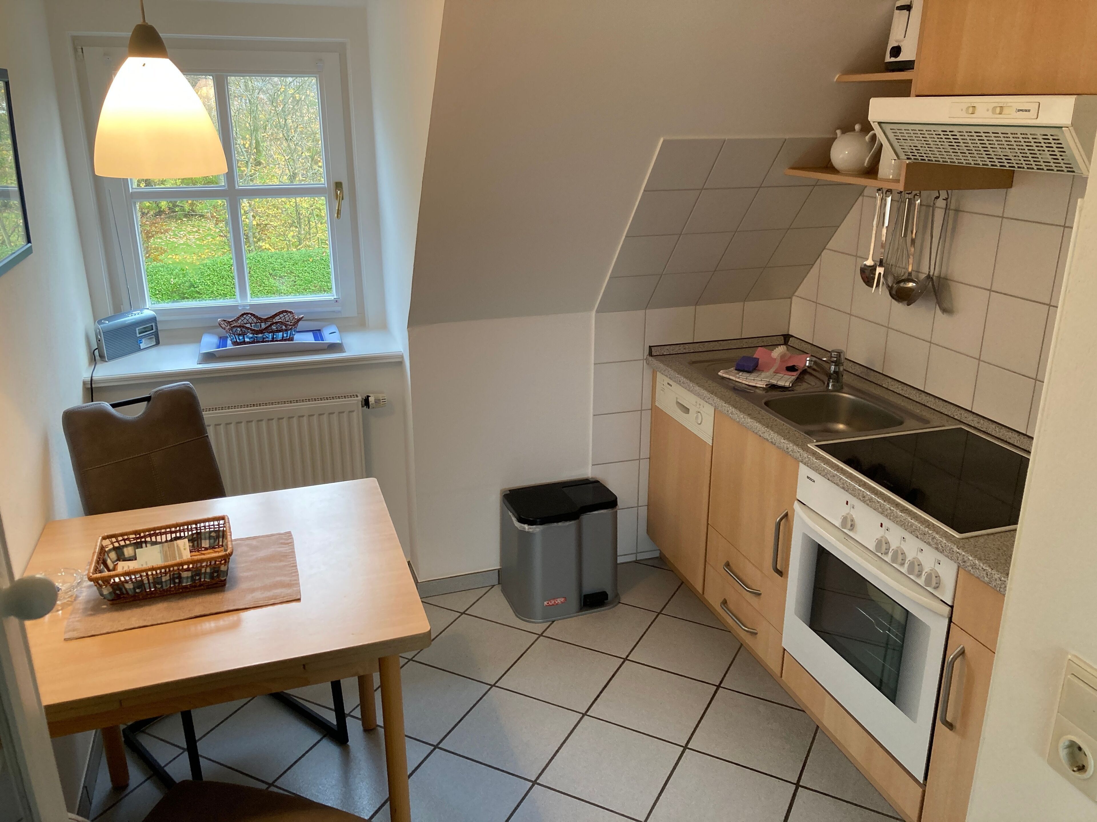 A kitchen with a dining table, a window with a view, a stove, a sink, and a trash bin.