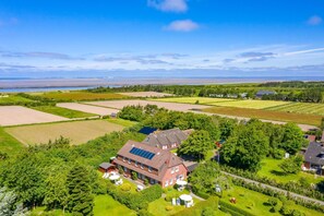 Une grande maison dotée de panneaux solaires, entourée d’une végétation luxuriante et de champs.