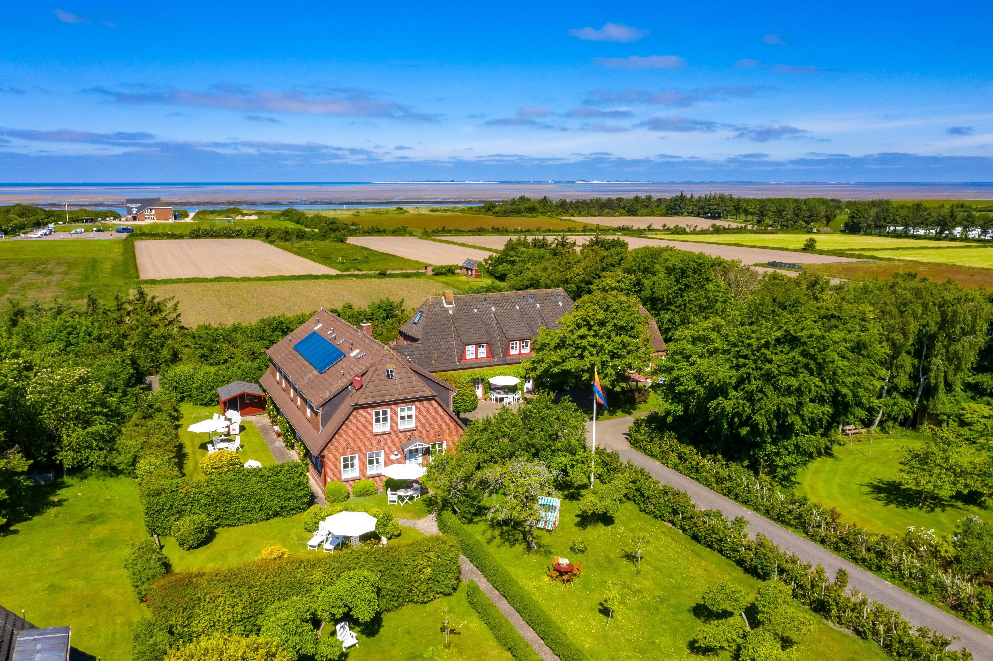 A large house with a solar panel, surrounded by well-maintained gardens and fields.