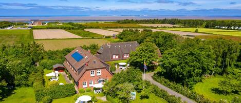 A large house with a solar panel, surrounded by well-maintained gardens and fields.