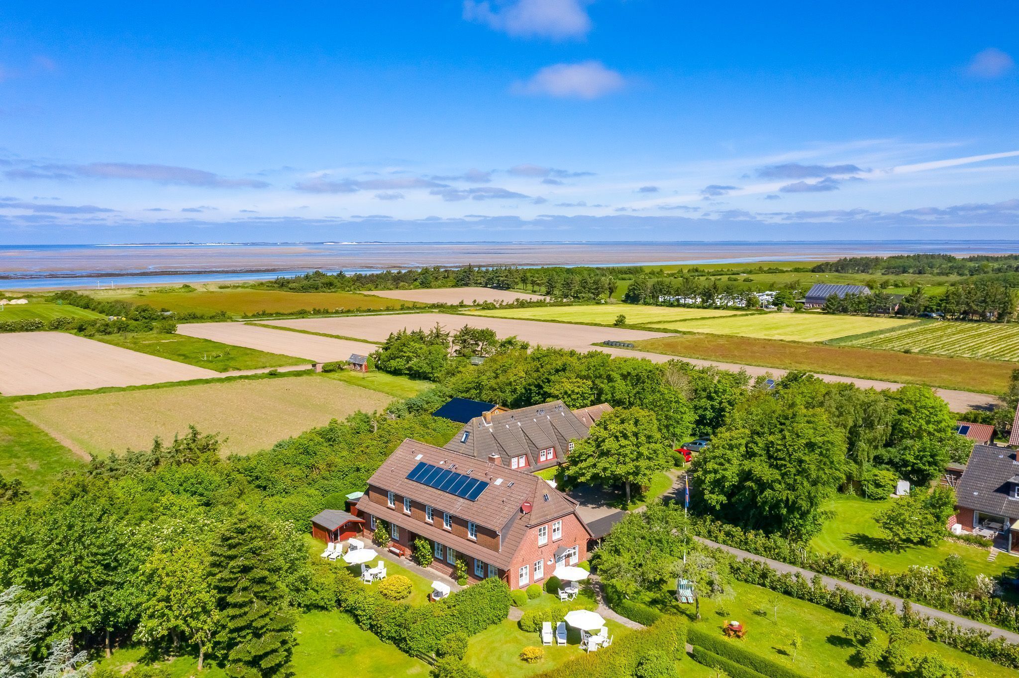 A large house with solar panels, surrounded by green fields and trees.