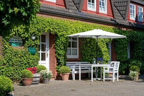 Un bâtiment en briques dont les murs sont recouverts de lierre, un banc blanc, une table et un parasol blanc.