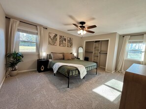A bedroom with a bed, bedside tables, a ceiling fan, a closet, and a window.