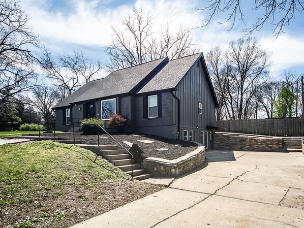 A modern two-story house with a dark exterior, a sloped roof, and a stone retaining wall.