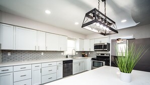 Une cuisine moderne avec des armoires blanches, un comptoir en marbre, un four encastré, un four à micro-ondes et un luminaire suspendu.