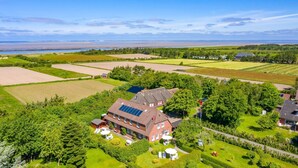 A large house with solar panels, surrounded by green fields and trees. - Whg. Pellworm - Haus am Deich (Utersum)
