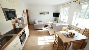 A modern kitchen with a dining area, a sofa, and a TV. - Whg. Pellworm - Haus am Deich (Utersum)