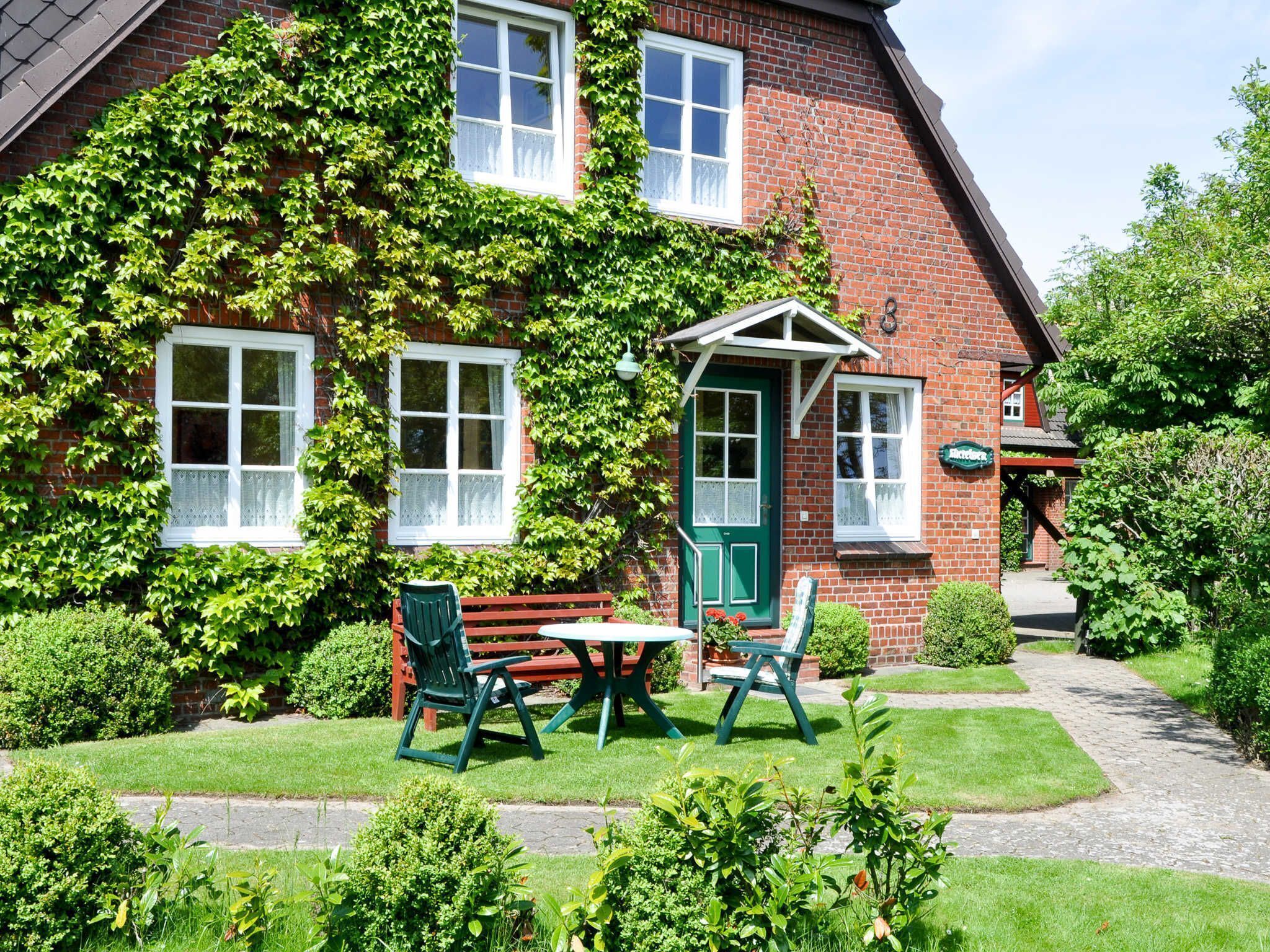 A brick house with ivy-covered walls, a green door, and a small garden with a bench and chairs.