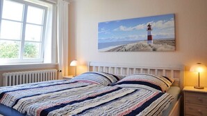 Une chambre à coucher avec un lit, un tableau représentant un phare, une fenêtre et un radiateur.