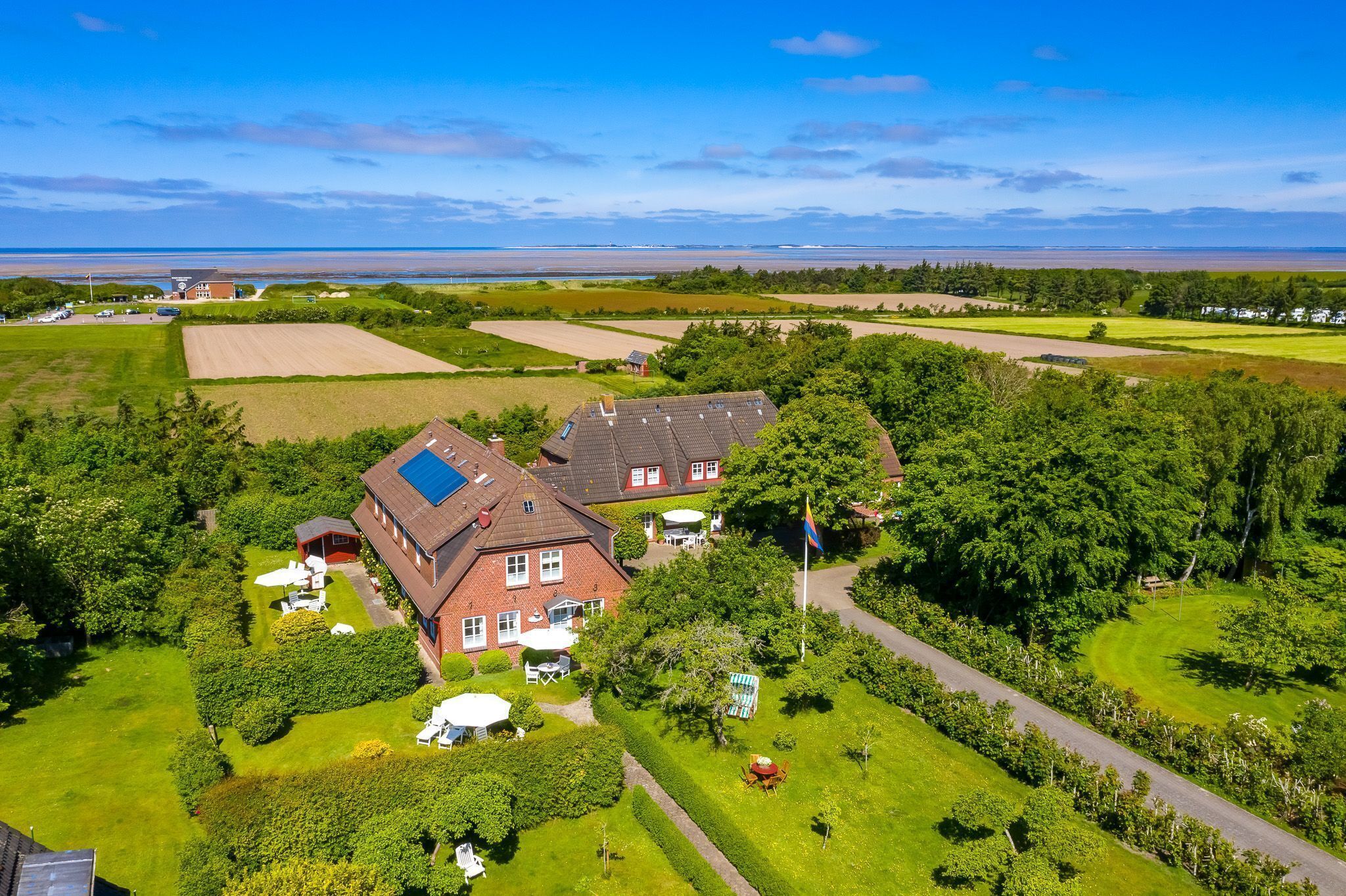 A large house with a solar panel, surrounded by well-maintained gardens and fields.