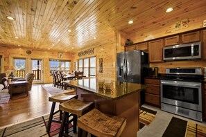 L’intérieur d’une cabane en bois comprend une cuisine équipée d’un réfrigérateur, d’un four à micro-ondes et d’un four traditionnel. On y trouve également un coin repas avec des chaises et une table, ainsi qu’un bar avec des tabourets.