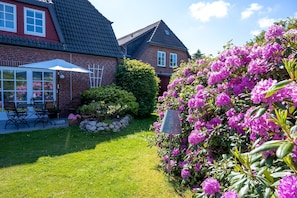 Una casa con facciata in mattoni, tetto rosso e un giardino con fiori rosa e un ombrello bianco.