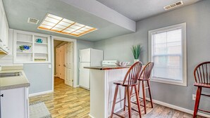 A compact kitchen with a central island, wooden chairs, a refrigerator, and a window with blinds.